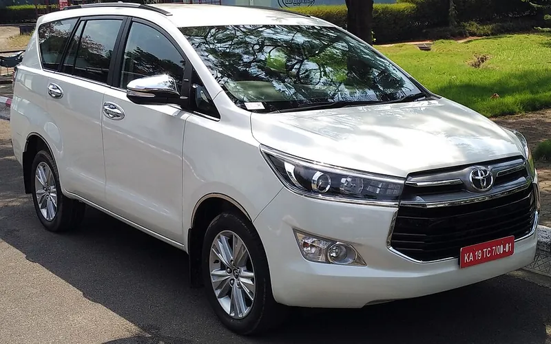 White Toyota Innova Crysta taxi with commercial yellow-on-black number plate, front three-quarter view